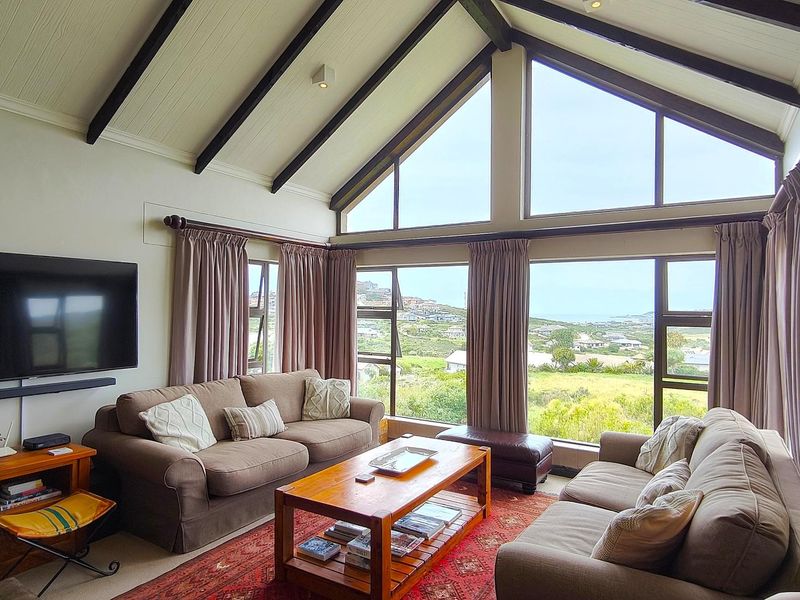 Spacious living room featuring a high vaulted ceiling with exposed timber beams and large windows offering expansive views of the surrounding landscape.