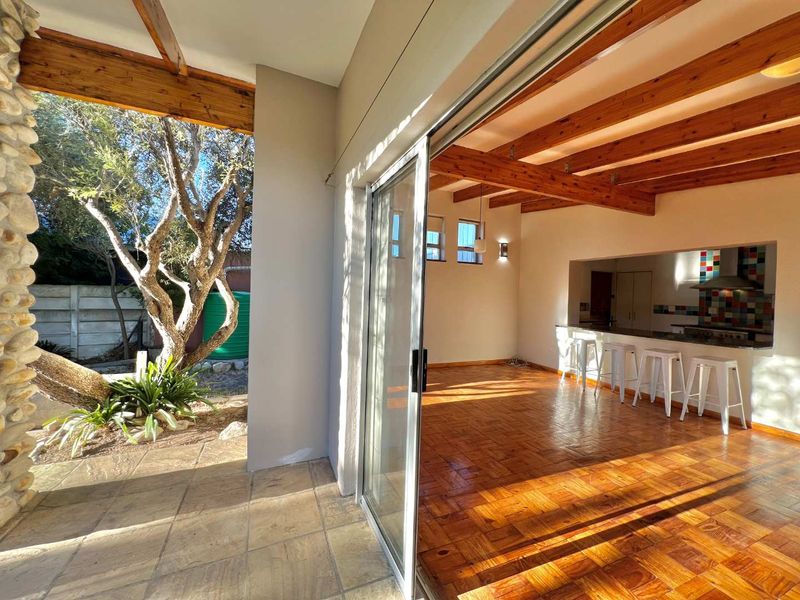 Spacious open-plan living area featuring warm parquet flooring, exposed timber beams, and seamless flow to a covered patio through large sliding glass doors.