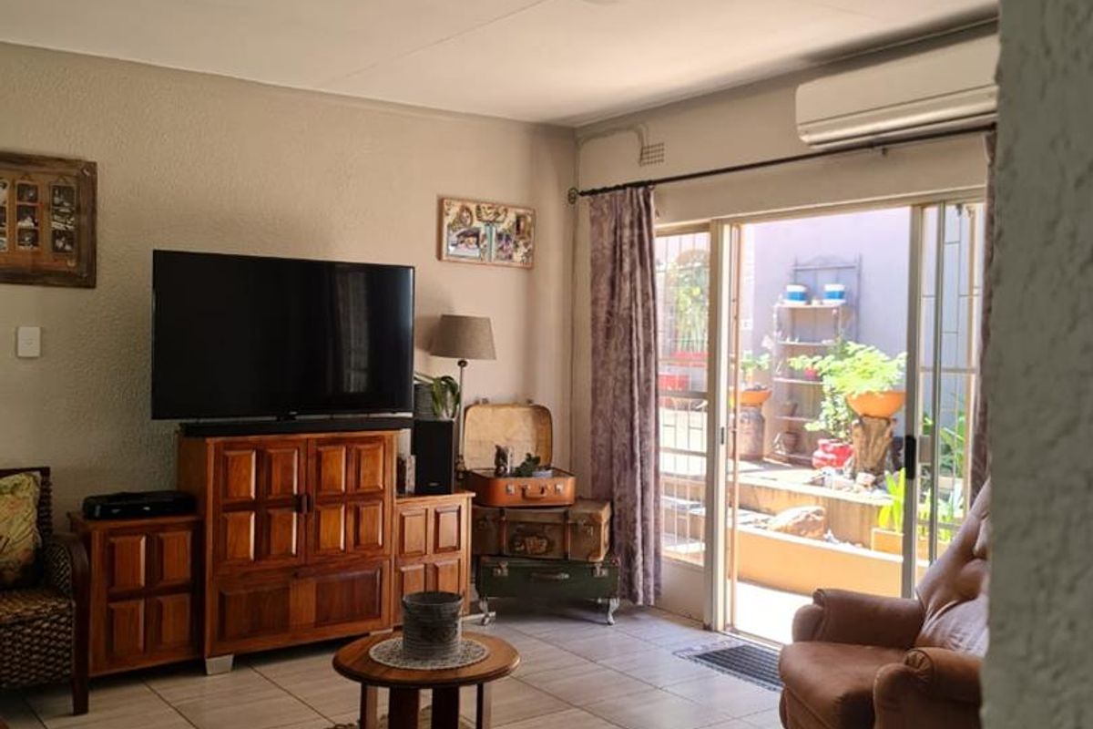 A comfortable living room featuring tiled flooring, a wall-mounted air conditioning unit, and sliding glass doors that open onto a private patio area.