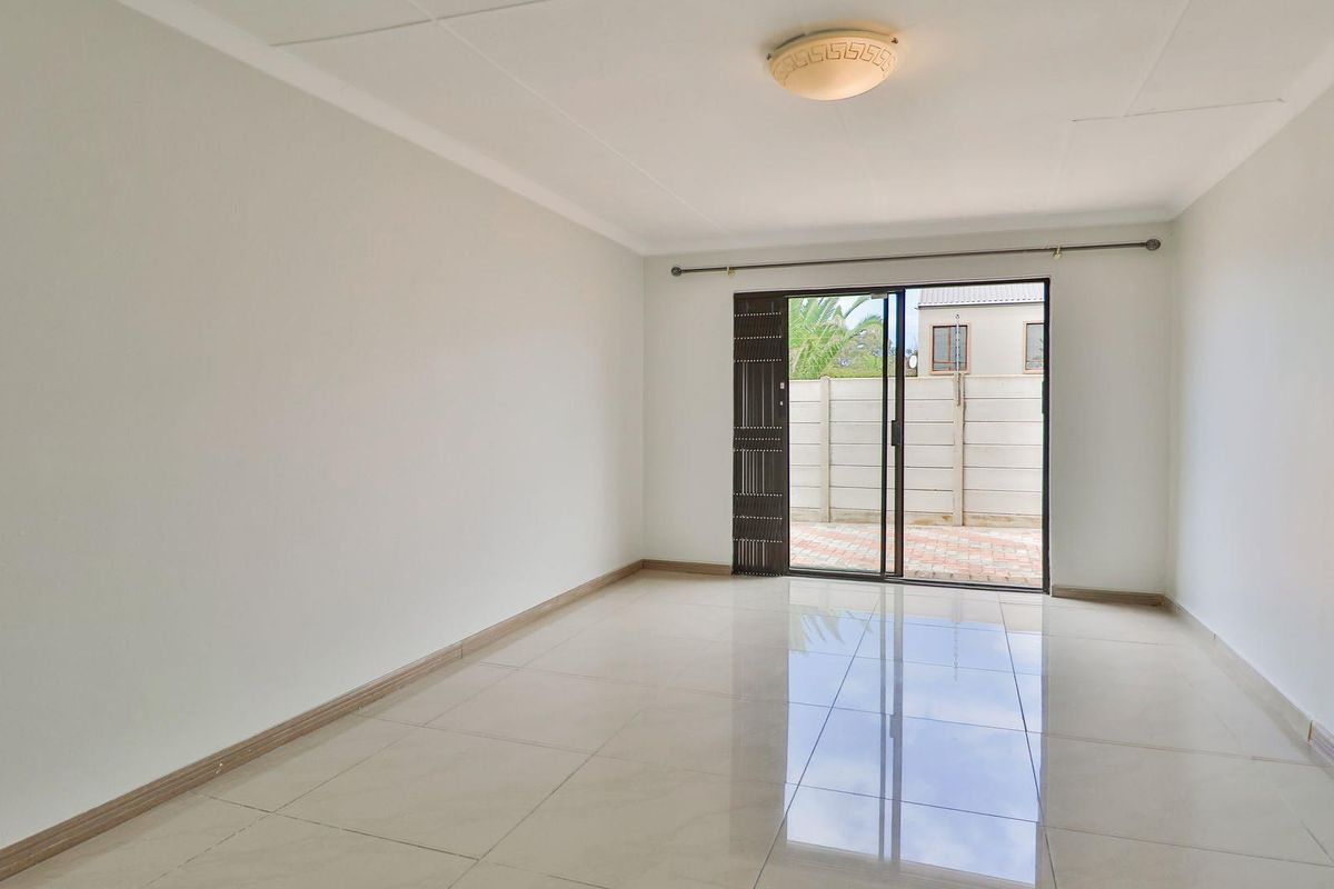 A bright, empty living room featuring polished floor tiles, a ceiling-mounted light fixture, and sliding glass doors leading to an outdoor patio area.