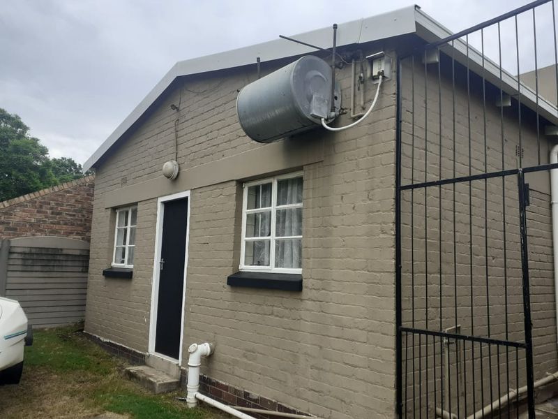Rear exterior view of the cottage featuring painted brick walls, security gate, and an externally mounted geyser unit.