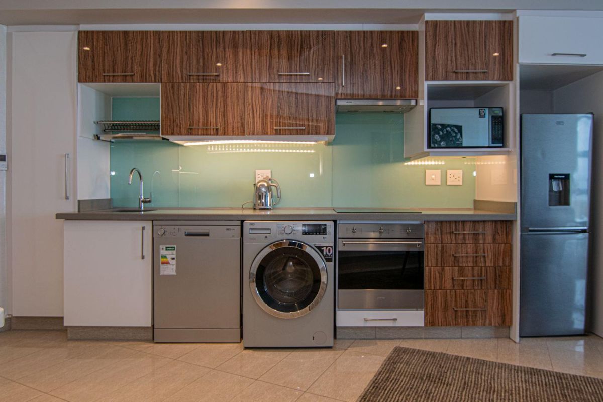 Modern kitchen featuring wood-grain cabinetry, glass splashback, integrated oven, hob, extractor fan, and dedicated spaces for a dishwasher and washing machine.