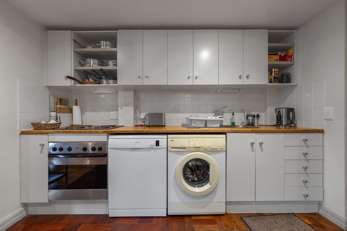 A functional kitchen featuring white cabinetry, a wooden countertop, tiled backsplash, and integrated appliances including an oven and hob.