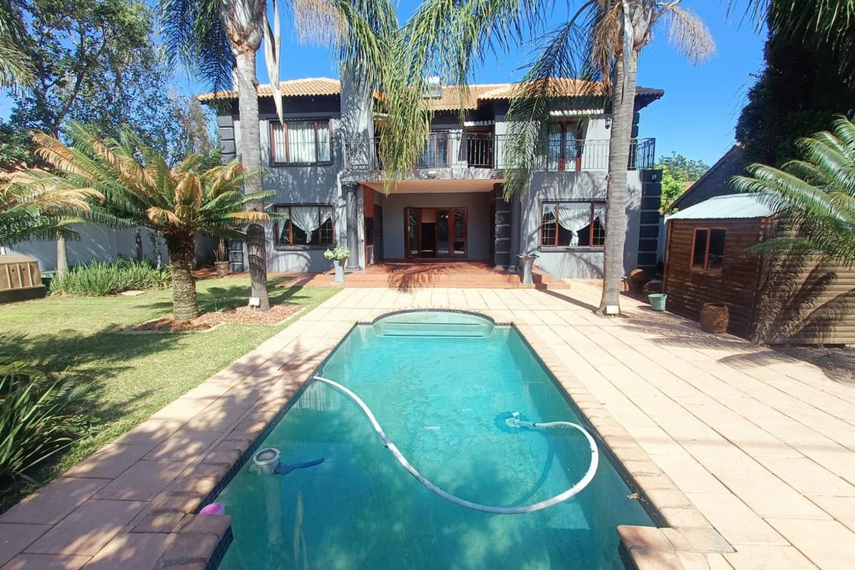 A spacious rear exterior view featuring a swimming pool, paved patio area, landscaped garden, and a two-story house with a balcony.