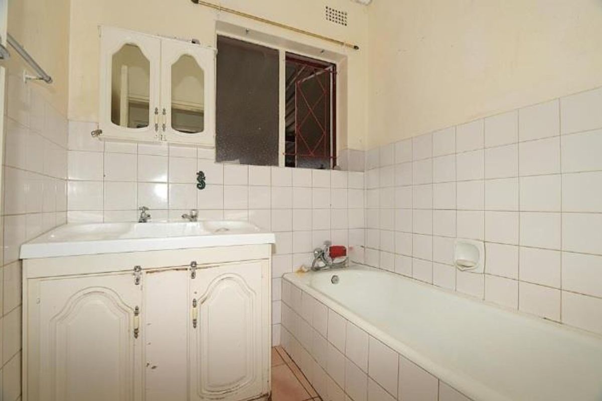 A dated bathroom featuring a built-in vanity cabinet, a standard bathtub with wall-mounted taps, and tiled wall finishes.