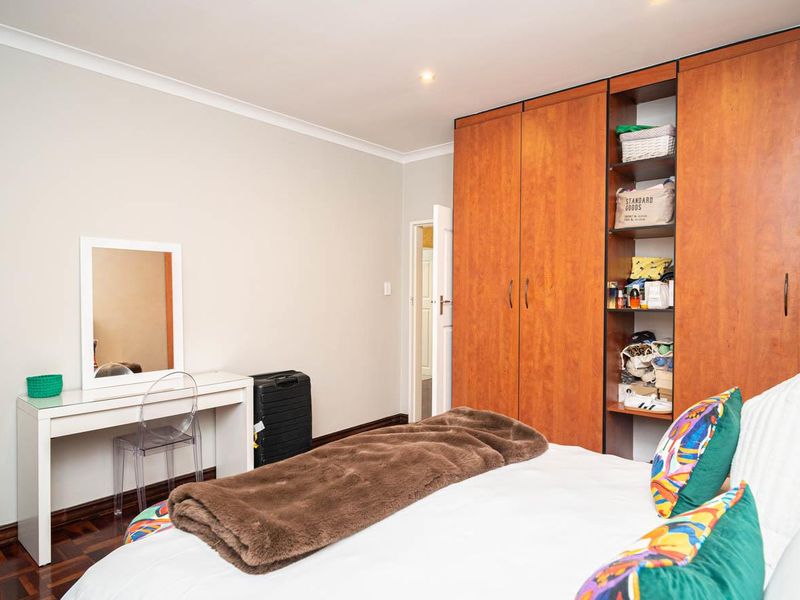 A well-maintained bedroom featuring warm parquet flooring, recessed ceiling lighting, and extensive built-in wooden wardrobe storage with integrated shelving.