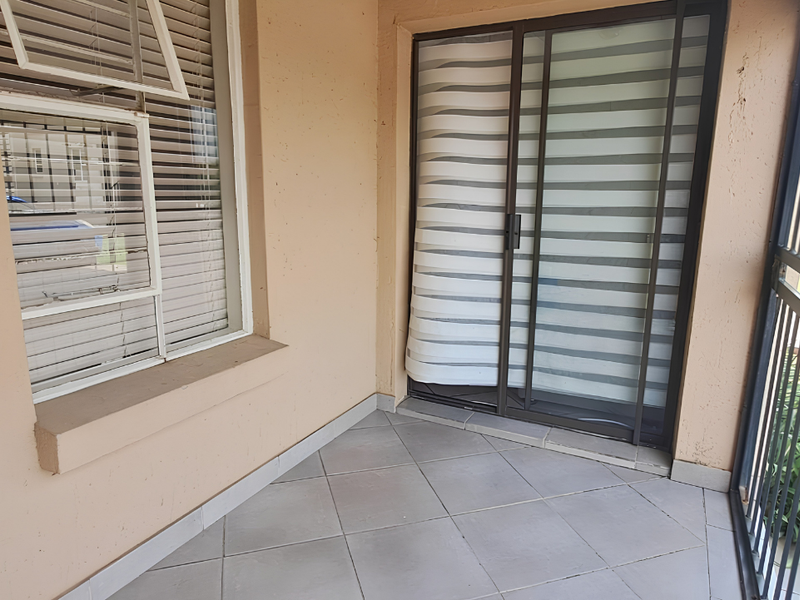 A covered patio area featuring tiled flooring, a sliding glass door, and a security gate, providing a functional outdoor space.