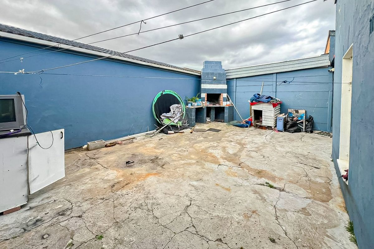 Rear courtyard area featuring a built-in braai, concrete paving, and enclosed boundary walls, requiring maintenance and surface repairs.