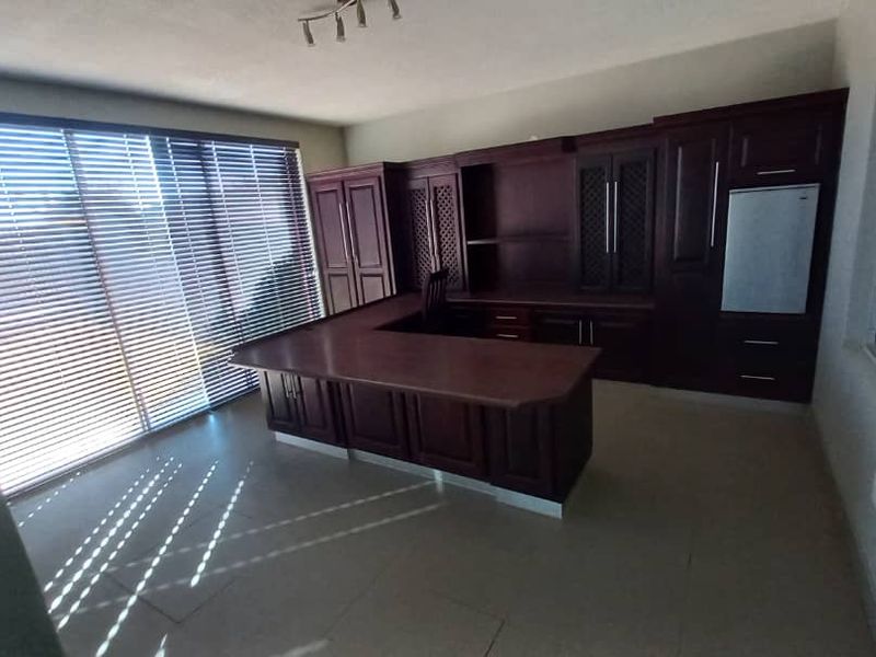 A professional office space featuring extensive built-in dark wood cabinetry, a large U-shaped desk, and large windows with venetian blinds.