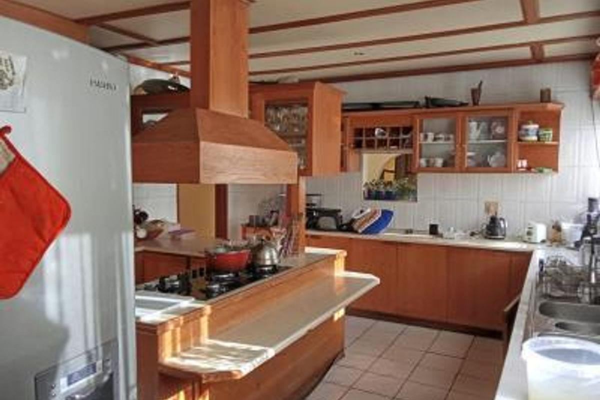 A spacious kitchen featuring extensive wooden cabinetry, a central island with a built-in hob and extractor fan, and tiled flooring throughout.