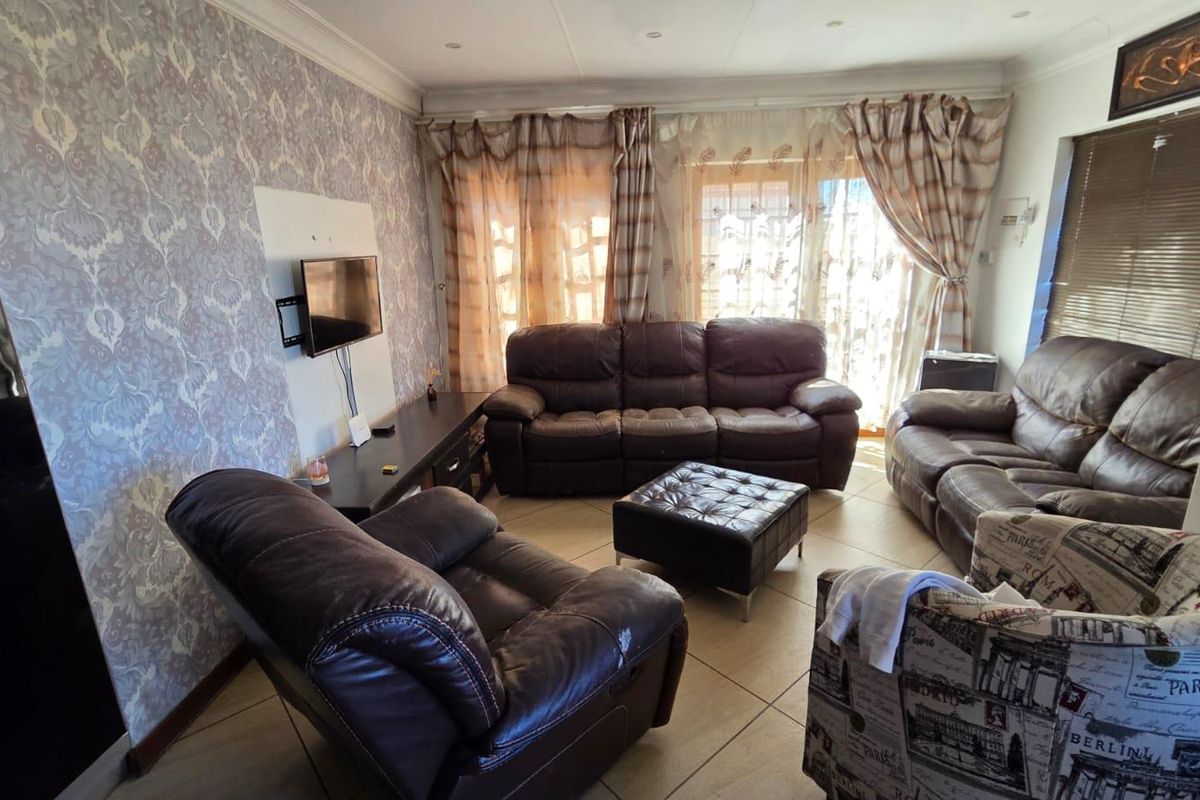 A comfortable living room featuring tiled flooring, patterned wallpaper, and large windows with curtains, providing a functional space for relaxation.