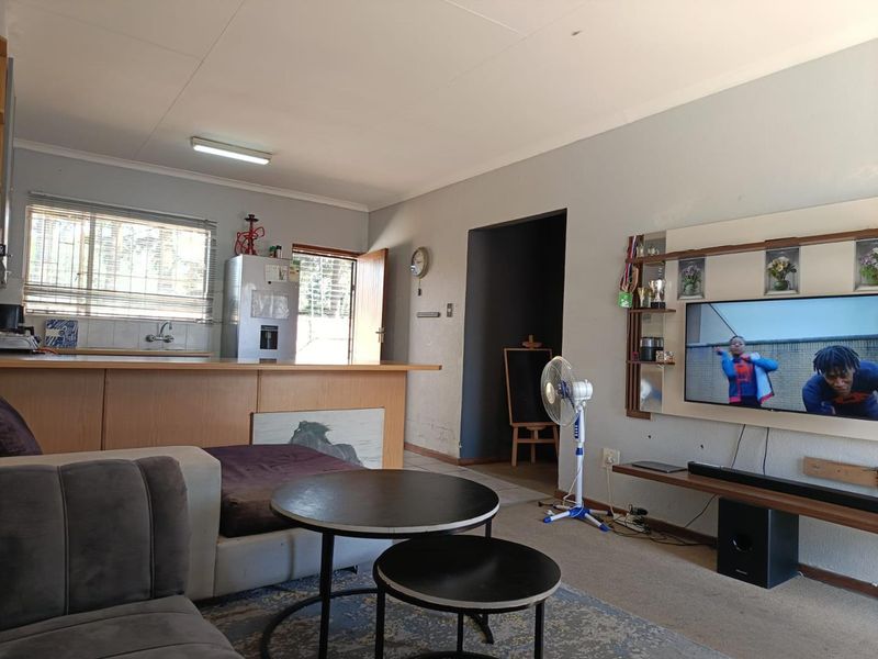 Open-plan living area featuring a kitchen with a breakfast bar, integrated sink, and built-in wall shelving, providing a functional layout for daily living.