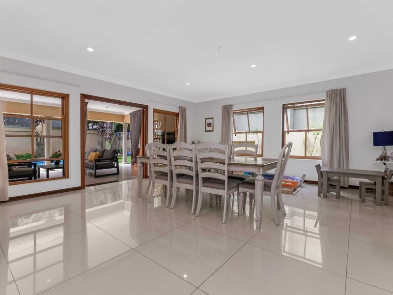 Spacious dining room featuring polished porcelain floor tiles, recessed downlighting, and large timber-framed windows and doors providing seamless access to the outdoor patio area.