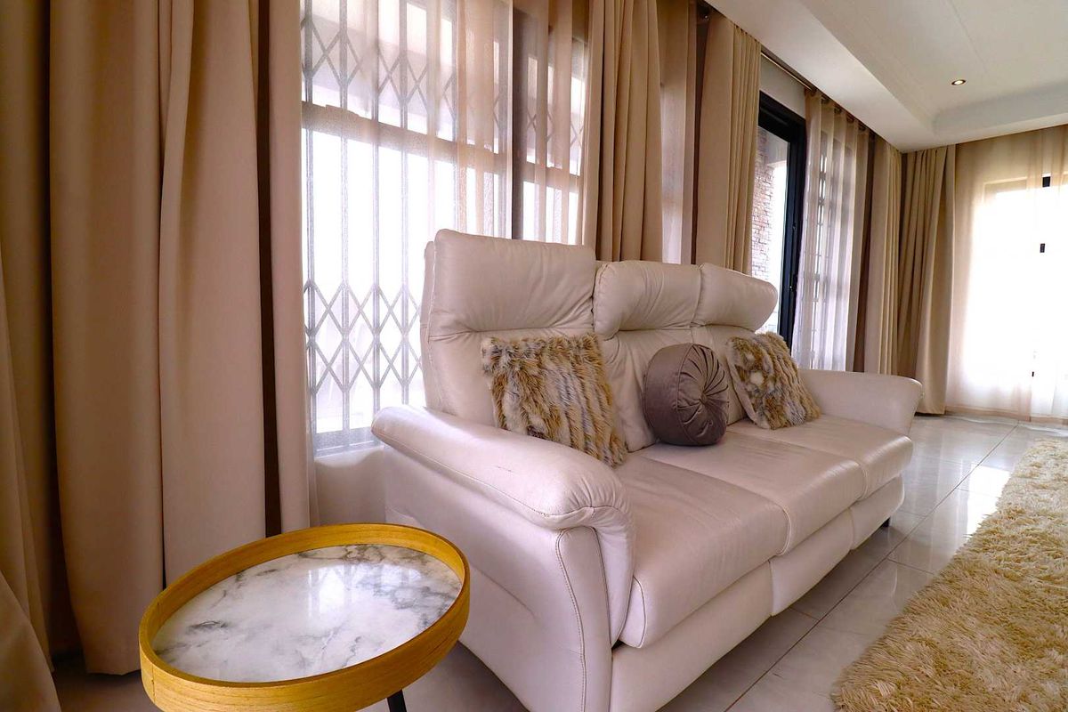 A bright living room featuring large windows with security gates, neutral tiled flooring, and recessed ceiling lighting.
