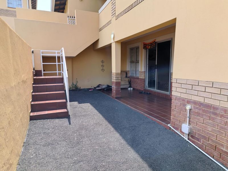 Rear exterior view of the townhouse featuring a covered tiled patio, external staircase with metal railing, and sliding glass door access.