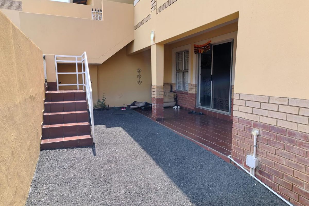 Rear exterior view of the townhouse featuring a covered tiled patio, external staircase with metal railing, and sliding glass door access.