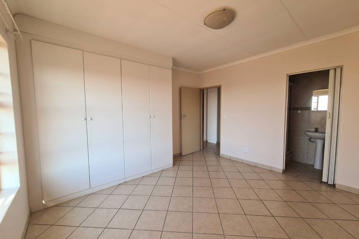 A spacious, empty bedroom featuring tiled flooring, built-in cupboards, and direct access to an en-suite bathroom.