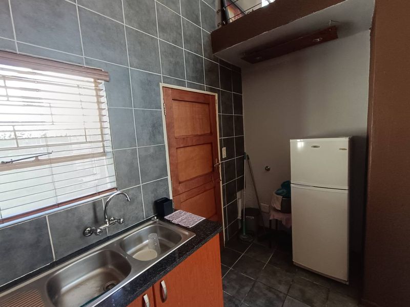 A functional kitchen area featuring a double bowl stainless steel sink, granite countertops, and dark tiled splashbacks with a wooden door.