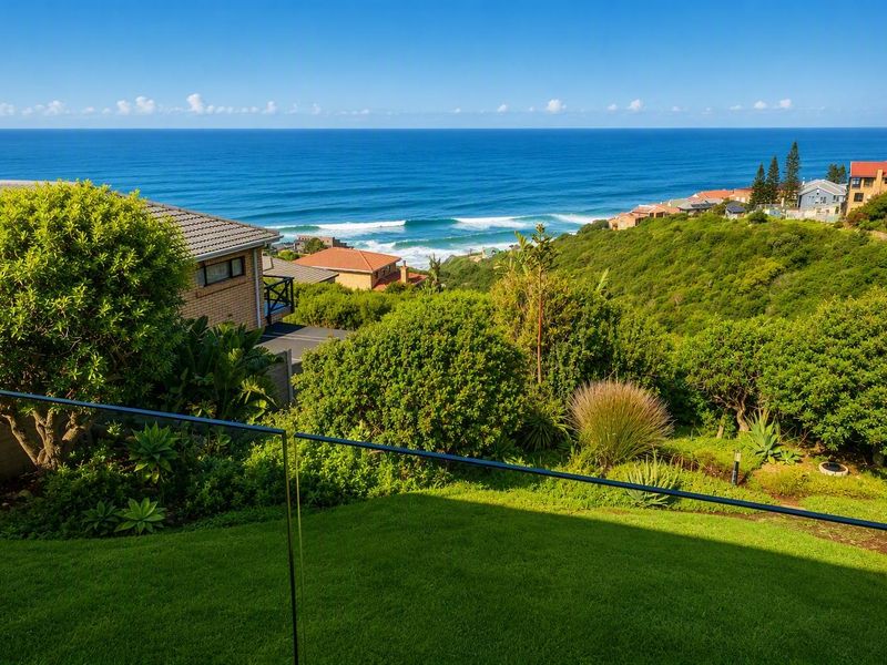 A stunning elevated coastal view overlooking the ocean, surrounding hillside residential properties, and lush green landscaping, framed by a modern glass balustrade.