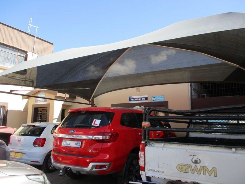 Industrial property exterior featuring a large shade cloth structure over a paved parking area with designated quotation bay signage.