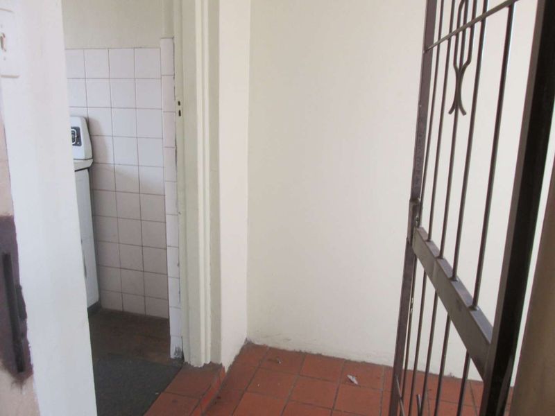 A utility or service area featuring tiled flooring, wall tiling, and a metal security gate, showing signs of wear and tear.