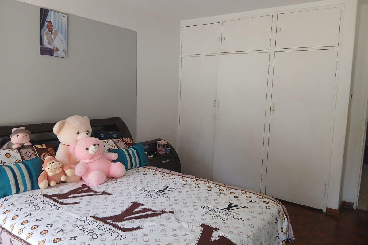 A bedroom featuring built-in floor-to-ceiling cupboards and dark wood-look flooring.