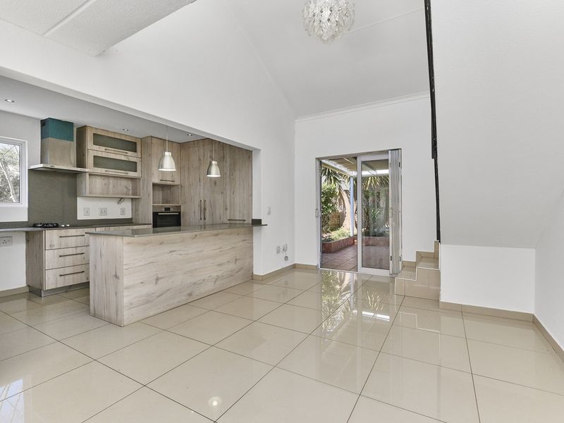Spacious open-plan kitchen and living area featuring modern wood-finish cabinetry, stone countertops, tiled floors, and direct access to an outdoor patio through sliding doors.