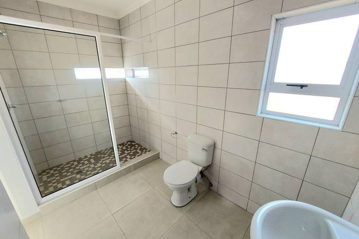A clean, modern bathroom featuring a glass-enclosed walk-in shower, tiled walls, a pedestal basin, and a standard toilet.