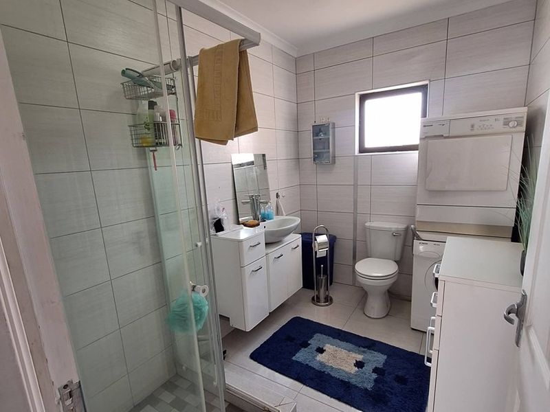 A functional bathroom featuring a glass shower enclosure, vanity basin, and toilet, finished with neutral wall and floor tiling.