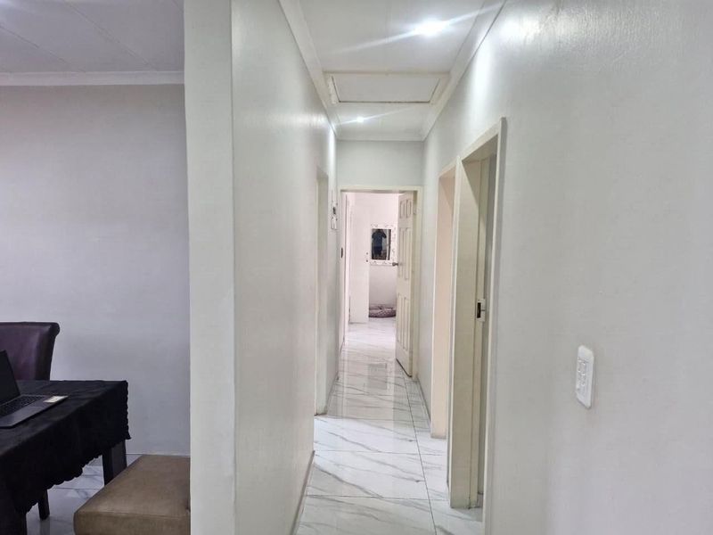 A bright, clean hallway featuring modern white marble-look floor tiles and recessed ceiling lighting, providing access to multiple rooms.