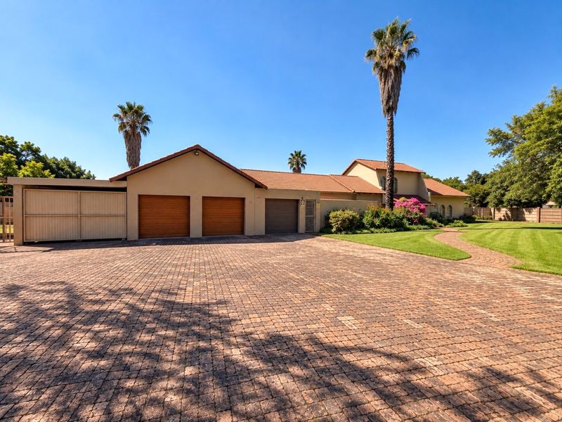 Spacious front exterior featuring a large paved driveway, triple garage, and well-maintained landscaped garden with mature palm trees.