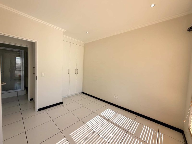 A bright, empty bedroom featuring neutral tiled flooring, built-in cupboards, and recessed downlighting, offering a clean and versatile space.