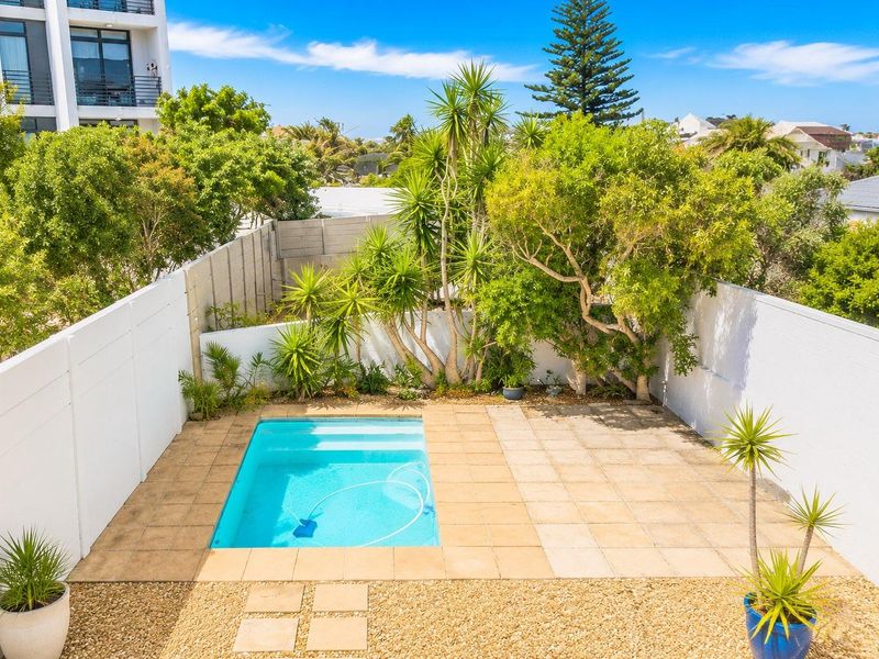 A private outdoor pool area featuring a paved deck, surrounding boundary walls, and established garden landscaping.