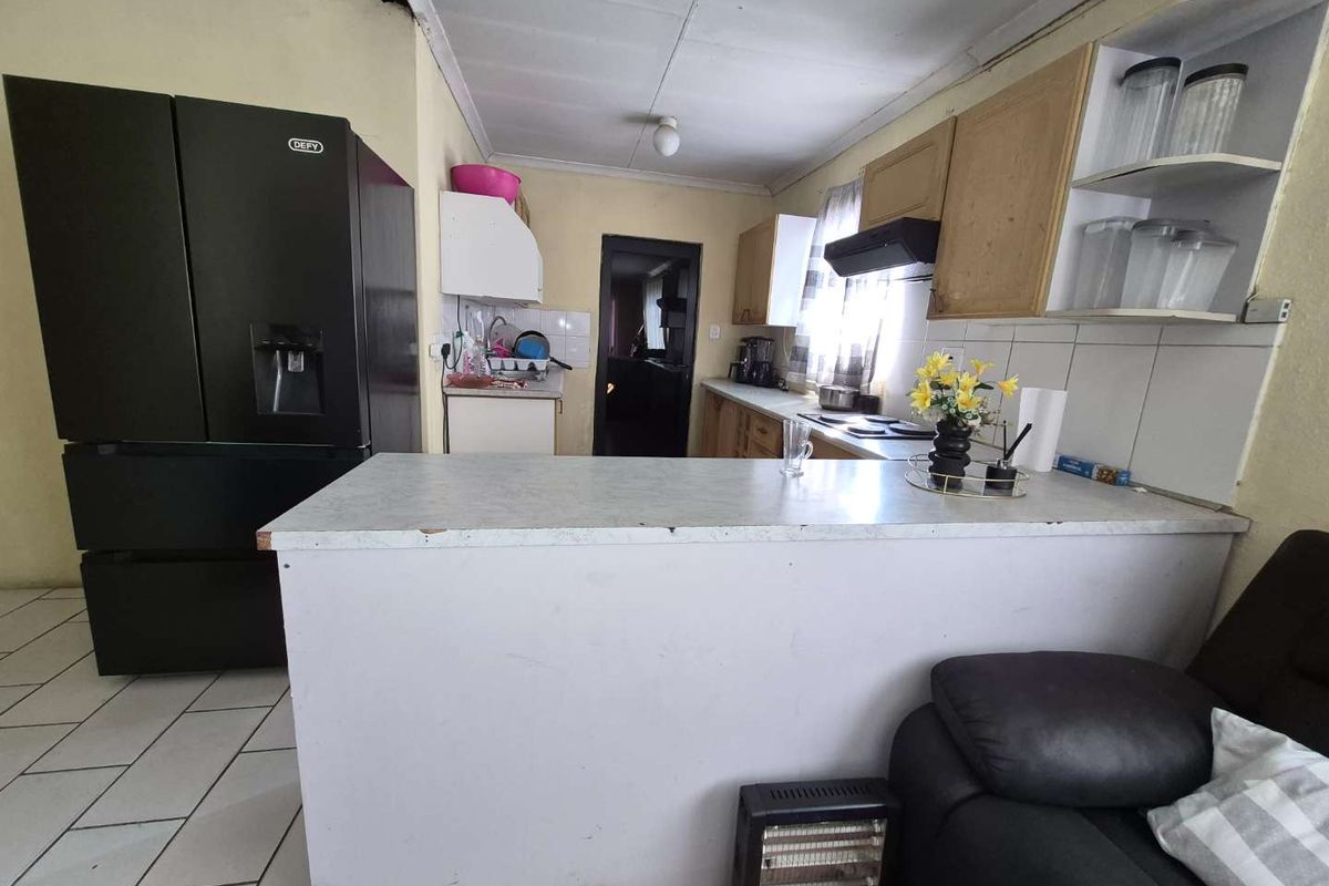 A dated kitchen featuring built-in cabinetry, a breakfast bar, and tiled flooring, currently showing signs of wear and ceiling damage.