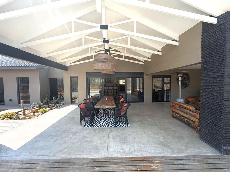 Spacious covered patio featuring exposed white timber roof trusses, concrete flooring, and a striking stone-clad feature wall, perfect for outdoor entertaining.