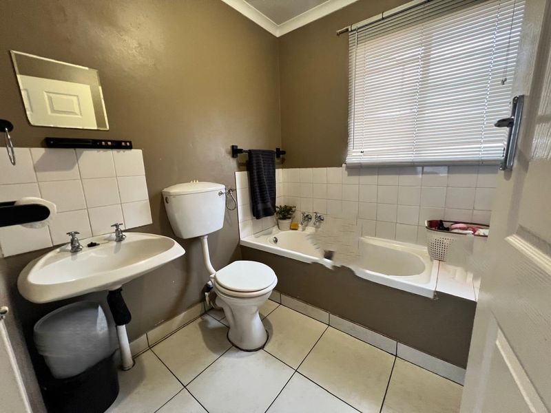 A functional bathroom featuring a pedestal basin, toilet, and built-in bathtub with tiled finishes, requiring some cosmetic updates to the wall and tub surround.