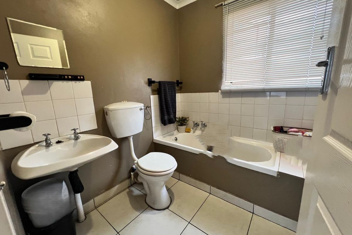 A functional bathroom featuring a pedestal basin, toilet, and built-in bathtub with tiled finishes, requiring some cosmetic updates to the wall and tub surround.