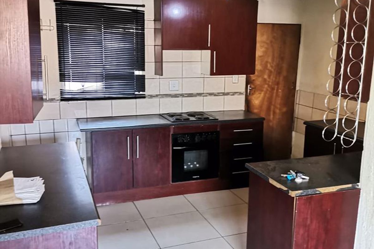 A functional kitchen featuring dark wood cabinetry, built-in oven and hob, tiled flooring, and a breakfast counter, offering a practical layout for daily use.