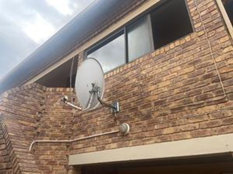 A view of the exterior face brick facade featuring a sliding window, mounted satellite dish, and external lighting fixture.