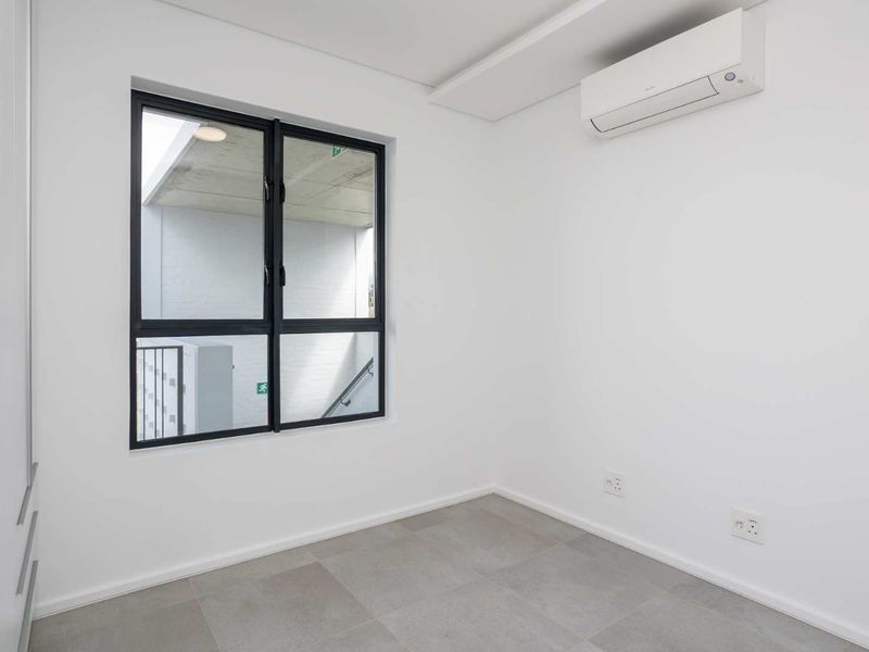 A bright, modern, and empty bedroom featuring tiled flooring, a built-in wardrobe, and a wall-mounted split-system air conditioner.