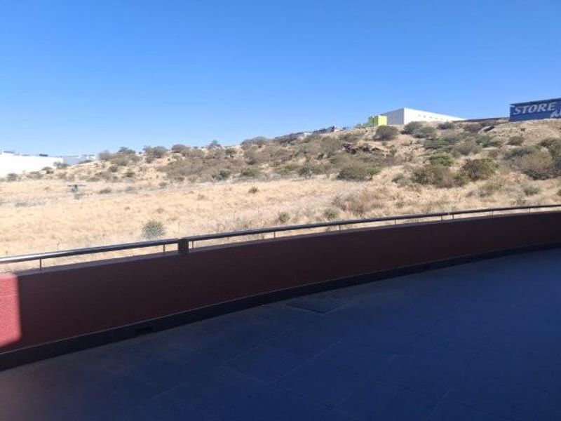 A spacious balcony with tiled flooring and a metal safety railing, offering an open view of the surrounding landscape.