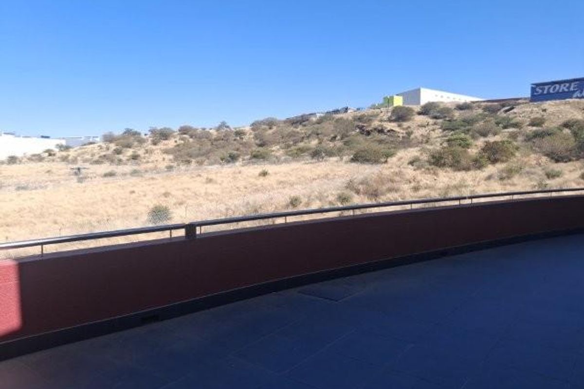 A spacious balcony with tiled flooring and a metal safety railing, offering an open view of the surrounding landscape.