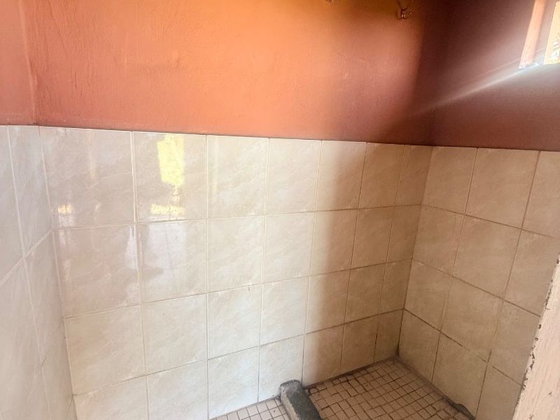 A basic shower enclosure featuring tiled walls and flooring, requiring renovation to update the finishes and improve the overall condition.