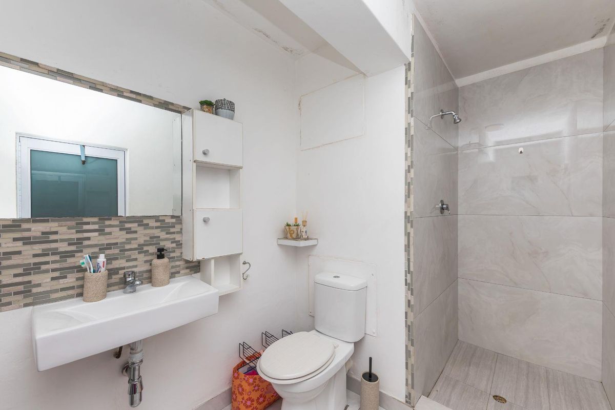 A functional bathroom featuring a wall-mounted basin, a toilet, and a walk-in shower with neutral large-format tiling and mosaic accents.