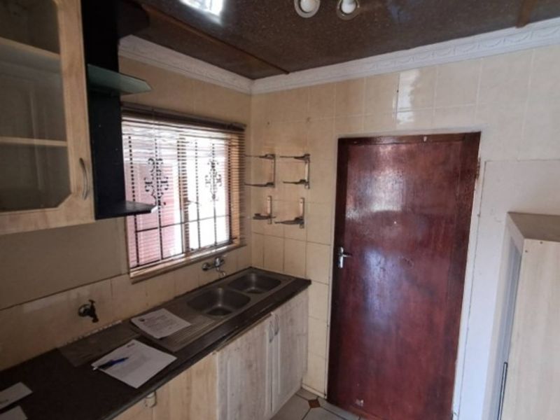 A compact kitchen featuring built-in cabinetry, a double bowl stainless steel sink, tiled splashbacks, and security bars on the window.