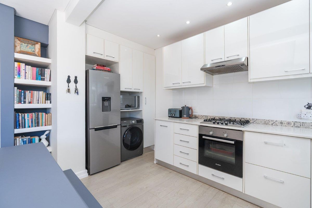 Modern kitchen featuring white cabinetry, gas hob, built-in oven, extractor fan, and integrated shelving, finished with light wood-look flooring.