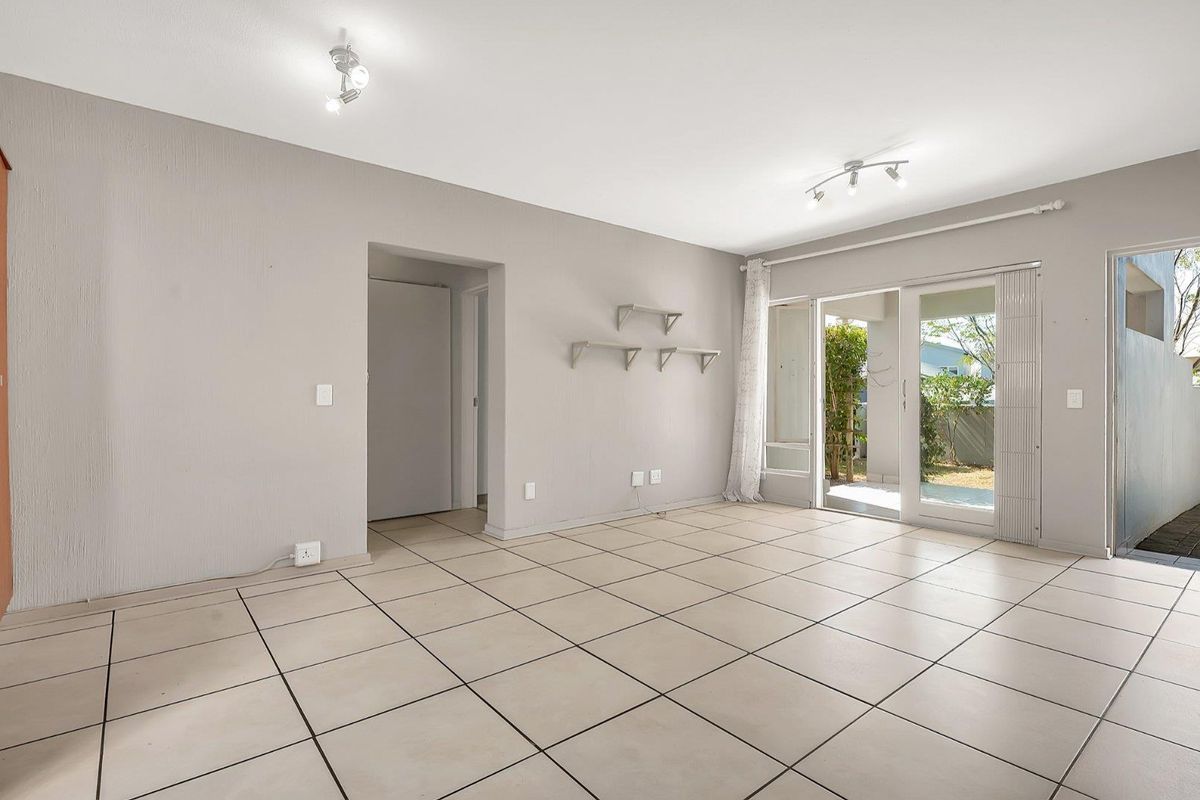 A bright, empty living room featuring neutral tiled flooring, wall-mounted shelving, and a sliding glass door providing access to the outdoor area.