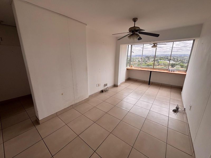 An empty bedroom featuring tiled flooring, a ceiling fan, and a large window with a built-in ledge offering expansive elevated views.