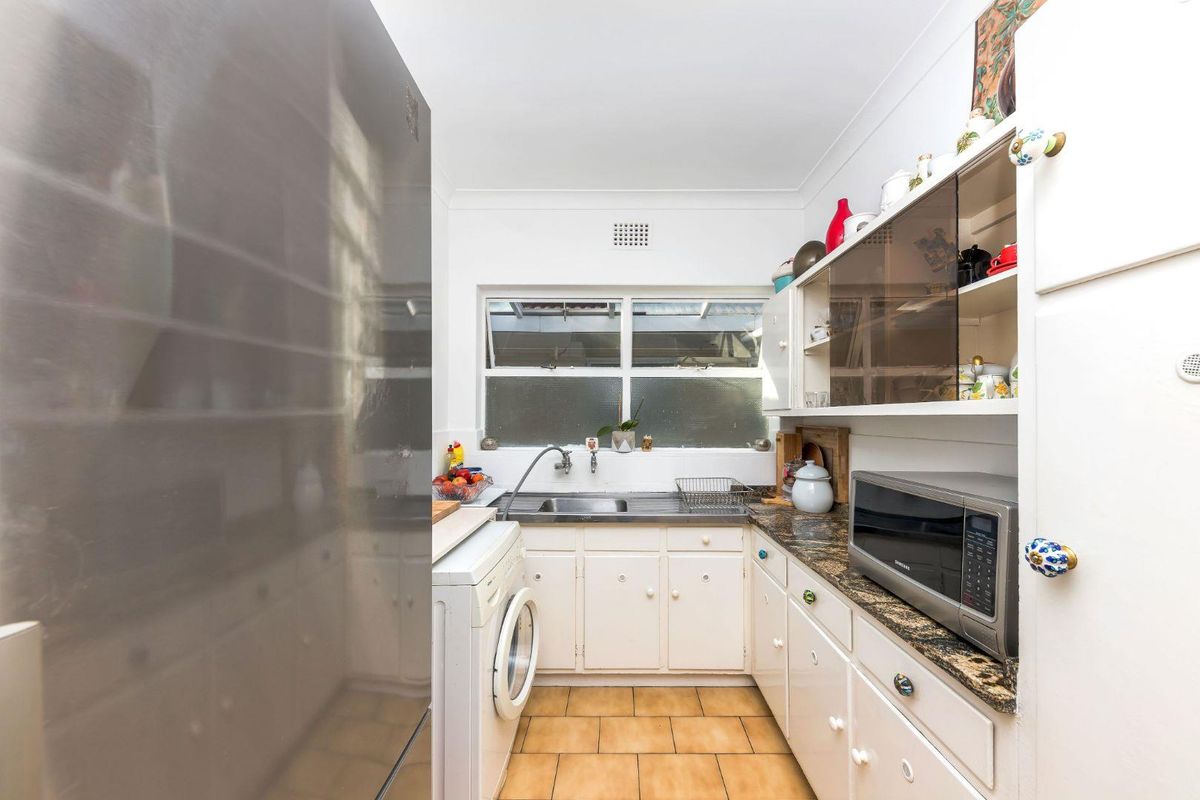 Compact kitchen featuring white cabinetry, laminate countertops, stainless steel sink, and tiled flooring, providing a functional space for daily meal preparation.