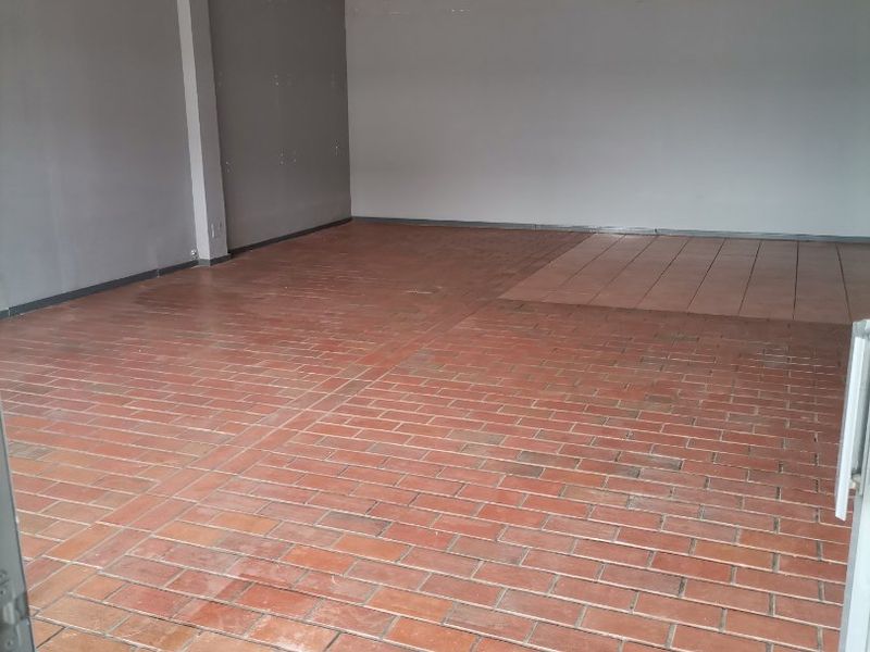 An empty, open-plan living area featuring a mix of terracotta and ceramic tile flooring with grey painted walls.